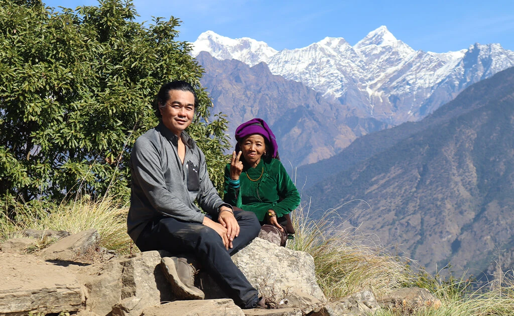 Client sitting on a stone ledge with local background snow-capped Himalayan mountains