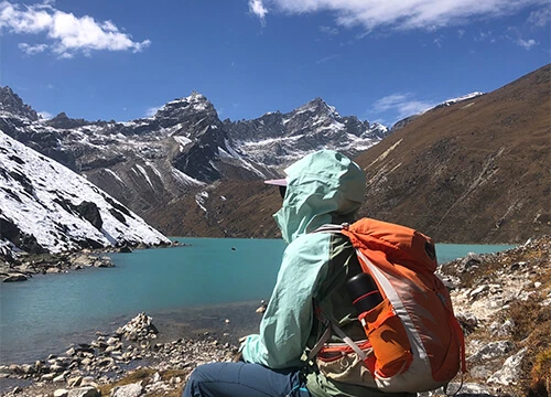 Trekker resting beside turquoise Gokyo Lake with snow-covered Himalayan mountains
