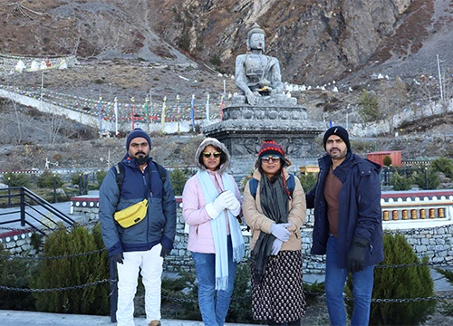 Four warm-dressed travelers posing in front of a Buddha statue in the mountains of Muktinath, Nepal.